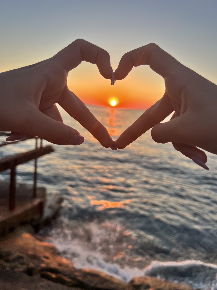 Hands forming a heart around the sun setting over the Mediterranean
